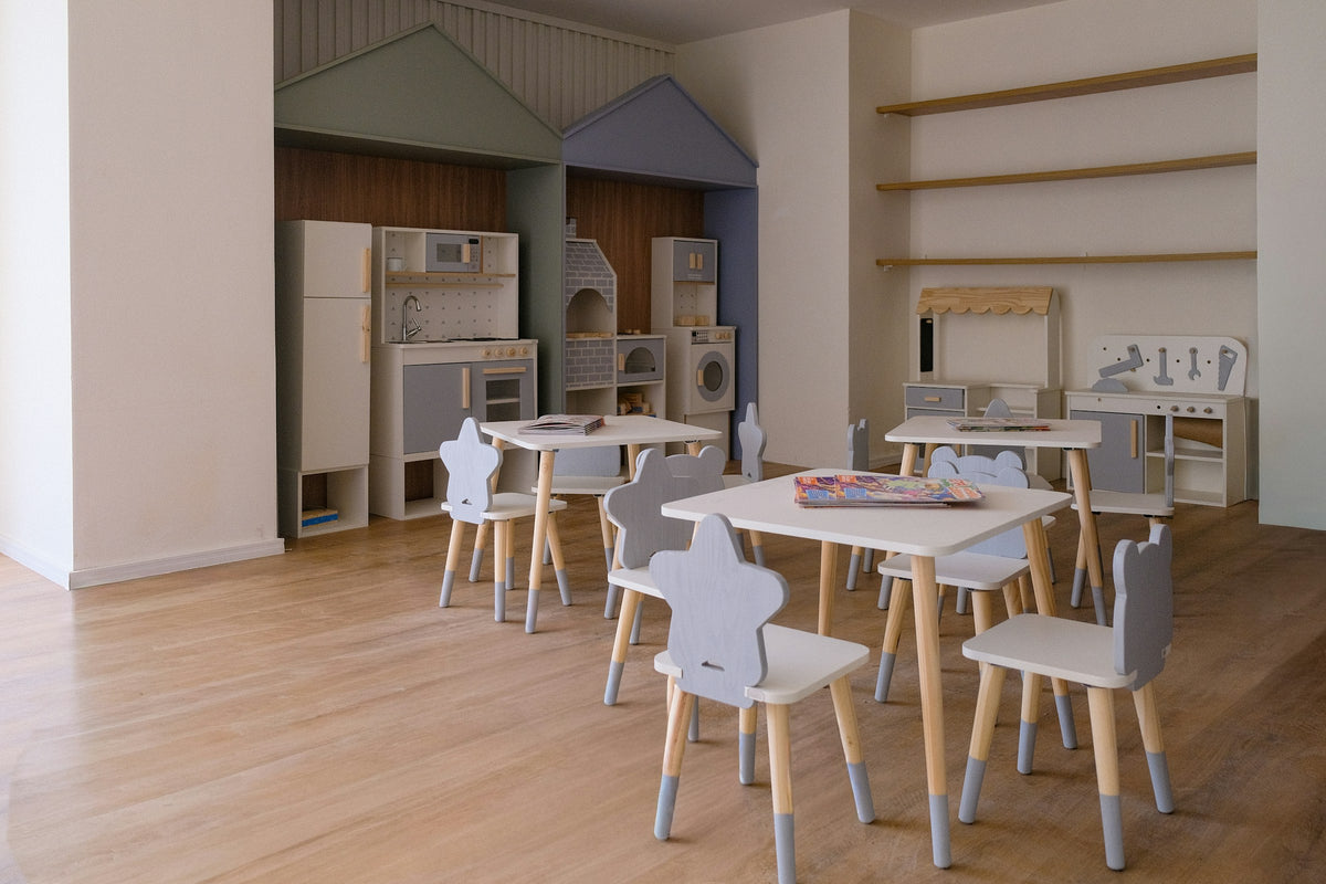 A tidy, light-filled children's playroom with small wooden tables and chairs