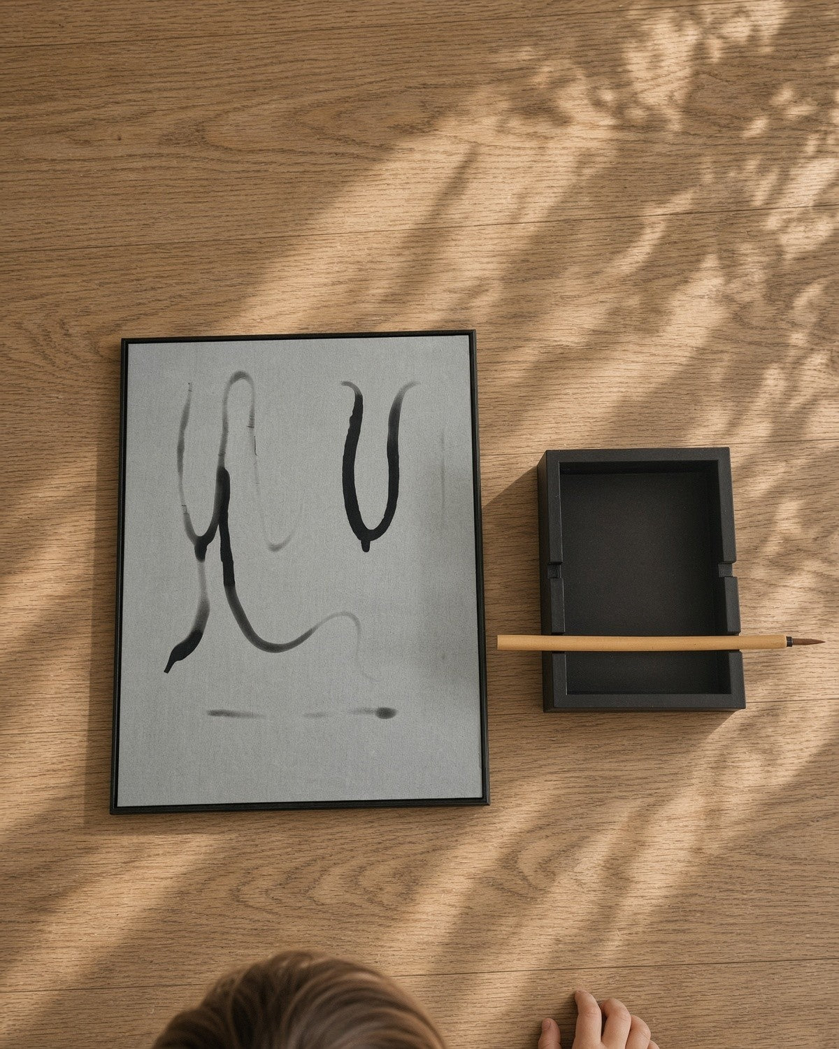 Seen from above, a child sits beside the board laid flat on a wooden floor, with the stand and brush next to it