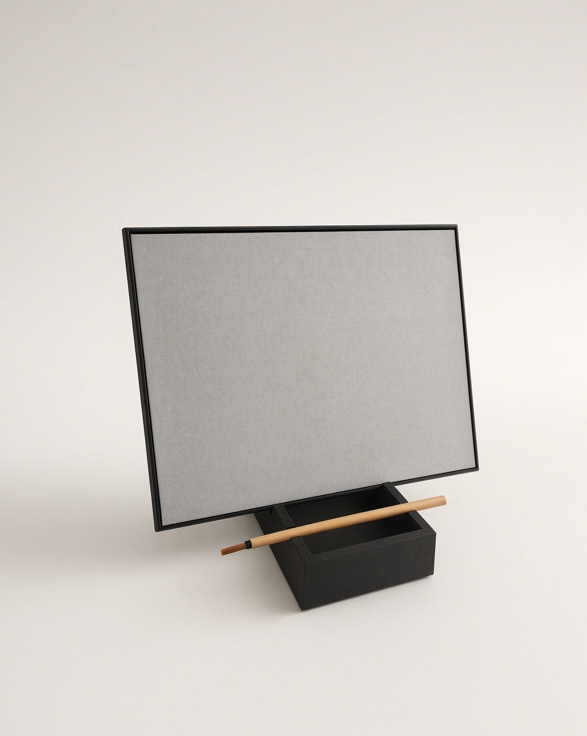 The blank grey board in landscape, slotted into its black stand with the brush across the front
