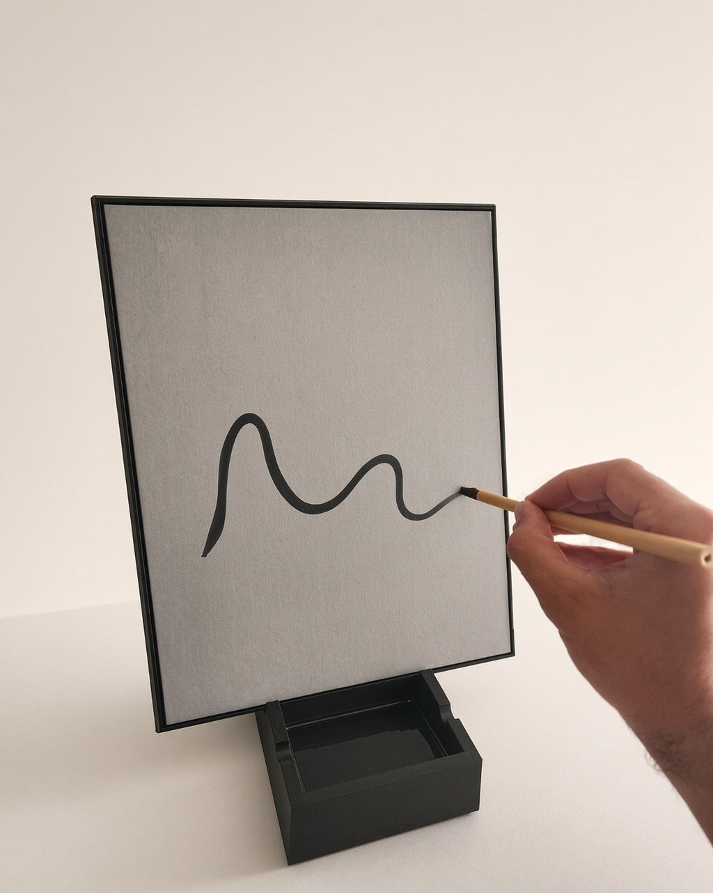A hand paints a wavy line onto the board with the bamboo brush, using only water