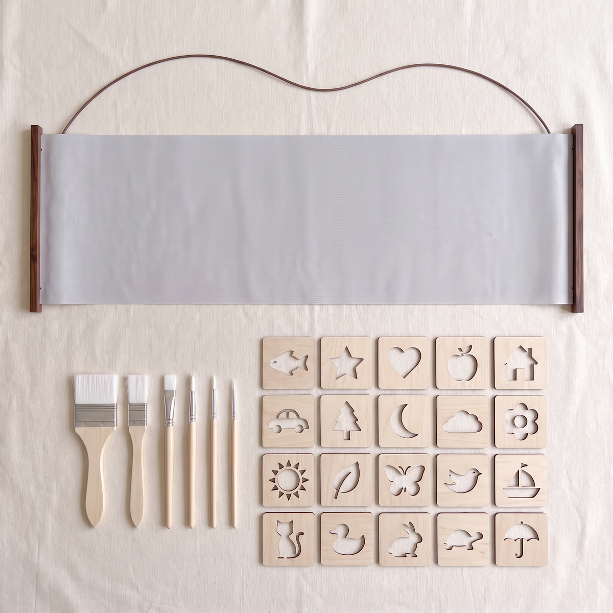 The Water Canvas part of the set laid flat: the long grey canvas on dark wooden rods with its cord, six wooden-handled brushes and twenty wooden stencils