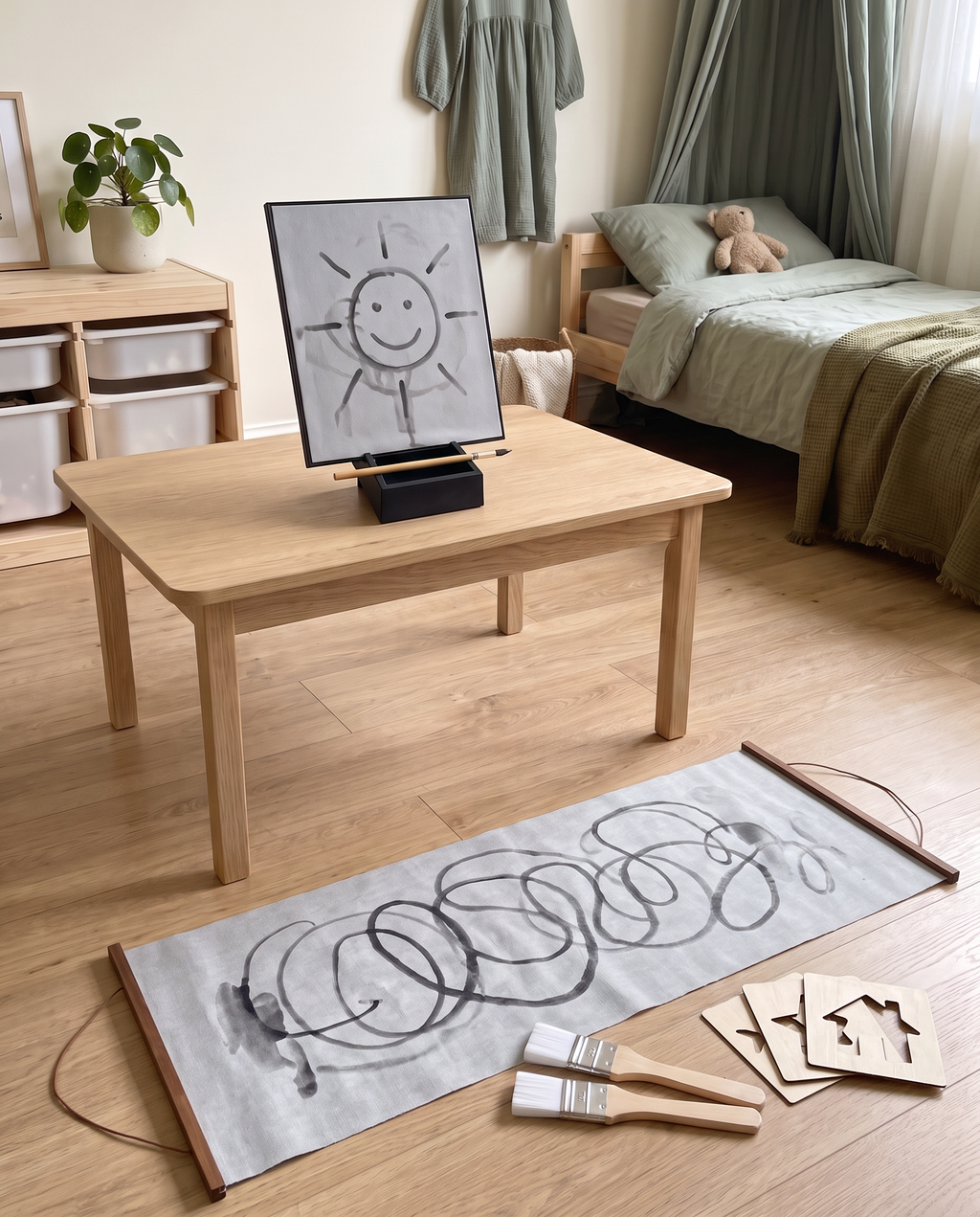The Water Easel on a kids' table with the Water Canvas laid flat on the floor in front of it, wooden rods at each end, brushes and wooden stencils beside it