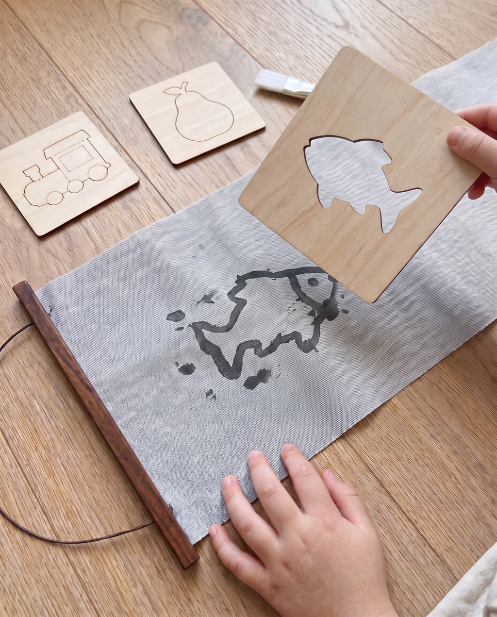 A wooden fish stencil lifts off the Water Canvas, revealing a water-painted fish underneath